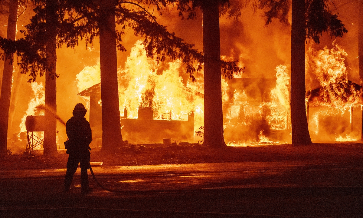 A firefighter sprays water on a propane tank as a home burns due to the Dixie Fire in the Indian Falls neighborhood of unincorporated Plumas county, California on July 24.
Inset: A firefighter crew poses for a picture as they put out hot spots near rustic mountain cabin homes in Twain, California on July 26. 
Photos: AFP