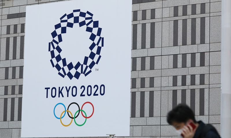 A man wearing protective face masks walk past the logo of the Tokyo 2020 Olympic Games displayed on a wall of The Tokyo Metropolitan Government Building in Tokyo, Japan, March 25, 2020.Photo:Xinhua

