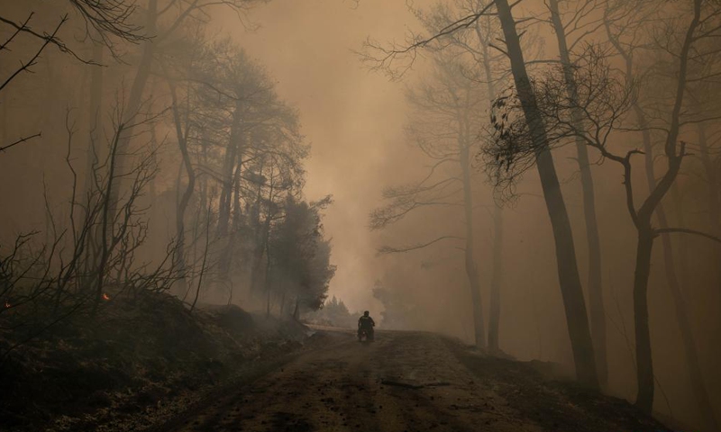 A man rides his motorcycle through the smog from a wildfire in the north of Evia island, Greece, on Aug. 5, 2021 . Greek Prime Minister Kyriakos Mitsotakis said on Thursday evening that Greece is facing an extremely critical situation with multiple forest fires at the same time, while saving human lives is the government's top priority.Photo:Xinhua