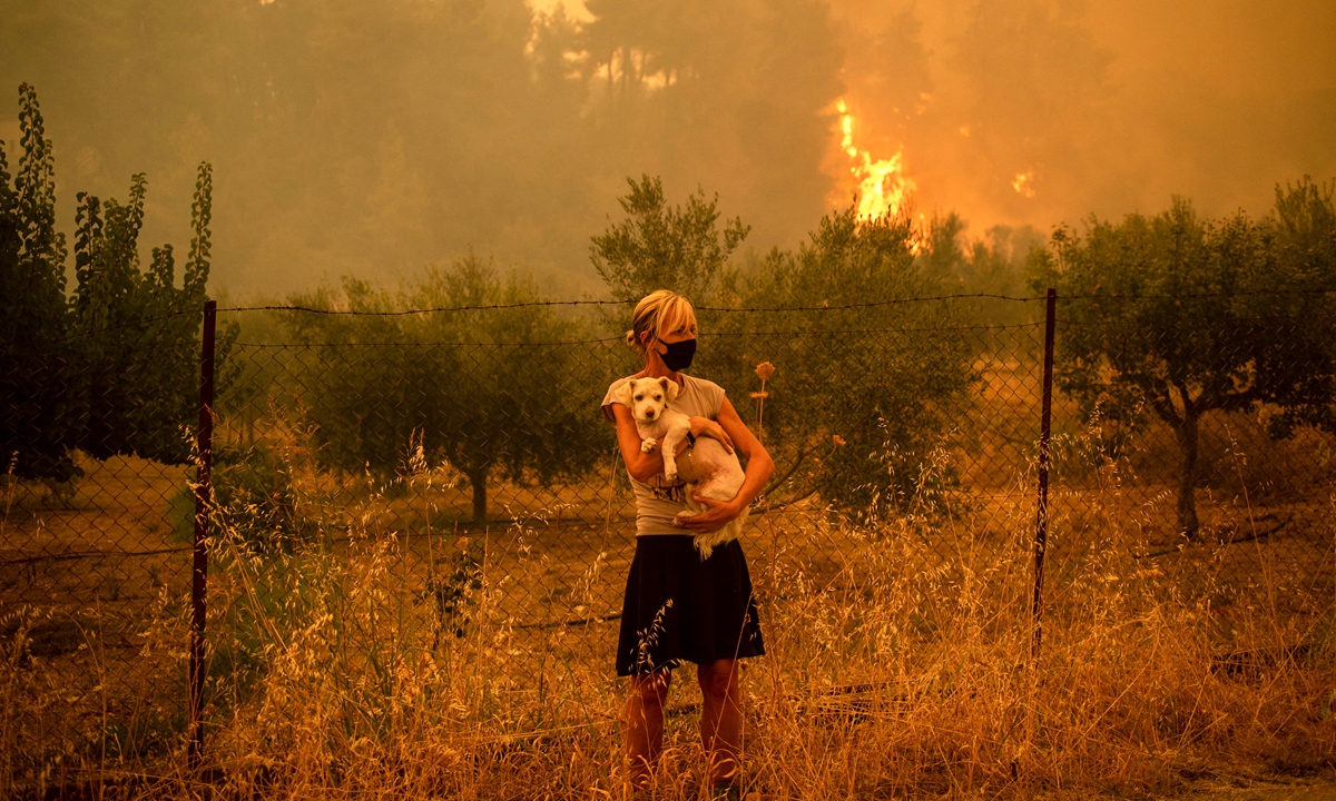 A woman holds a dog in her arms as forest fires approach the village of Pefki on Evia island, Greece on August 8. Greece and Turkey have been battling devastating fires for nearly two weeks as the region suffered its worst heatwave in decades, which experts have linked to climate change. Photo: AFP