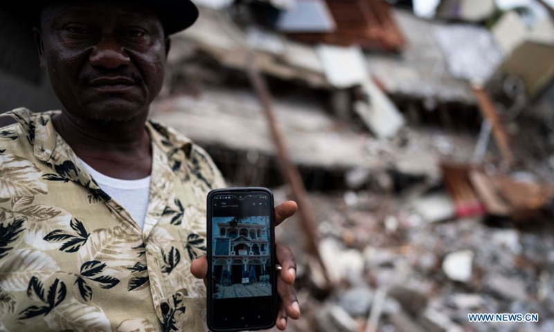 Franel Etienne shows a photo of his hotel before the earthquake in front of the debris of his hotel after an earthquake, in Les Cayes, Haiti, on Aug. 17, 2021. The death toll from a powerful earthquake that struck southwest Haiti on Saturday climbed to 1,941, the Caribbean island's Civil Protection Agency reported on Tuesday. (Xinhua/David de la Paz)