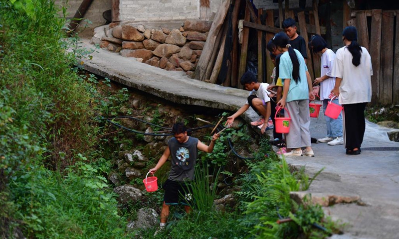 Colloge student Pan Wenbo (1st, L) cleans watercourse with local students at Wuying Village, which lies on the border between south China's Guangxi Zhuang Autonomous Region and southwest China's Guizhou Province, on Aug. 20, 2021. In the summer of 2021, a volunteer team consisted of college and middle school students led local pupils to participate in diverse activities, such as maintaining saplings, learning about intangible cultural heritages and collecting old farm tools for museums. (Xinhua/Huang Xiaobang)