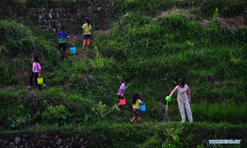 Colloge student Pan Muzhi (1st R) waters saplings with local pupils at Wuying Village, which lies on the border between south China's Guangxi Zhuang Autonomous Region and southwest China's Guizhou Province, on July 14, 2021. In the summer of 2021, a volunteer team consisted of college and middle school students led local pupils to participate in diverse activities, such as maintaining saplings, learning about intangible cultural heritages and collecting old farm tools for museums. (Xinhua/Huang Xiaobang)