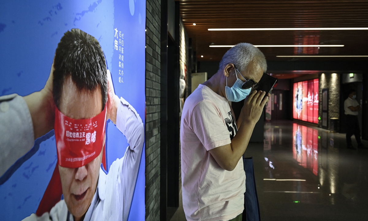 Visually impaired massage therapist Zhang Xinsheng uses his phone in front of a billboard supporting blind people at a cinema in Beijing on August 7. Photo: AFP