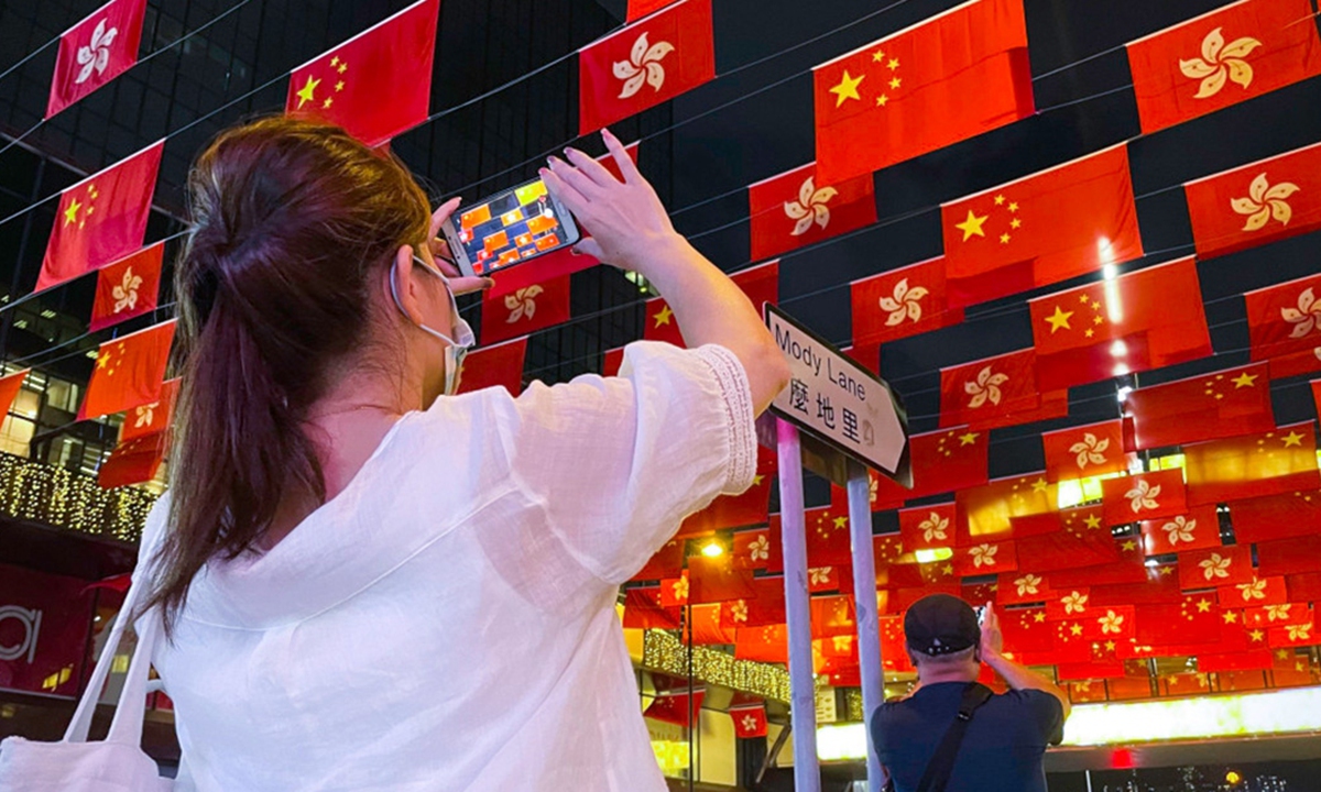A woman takes photos of the China's national flags and the flags of the Hong Kong Special Administrative Region in Tsim Sha Tsui, Hong Kong, on June 29. Photo: the Paper
