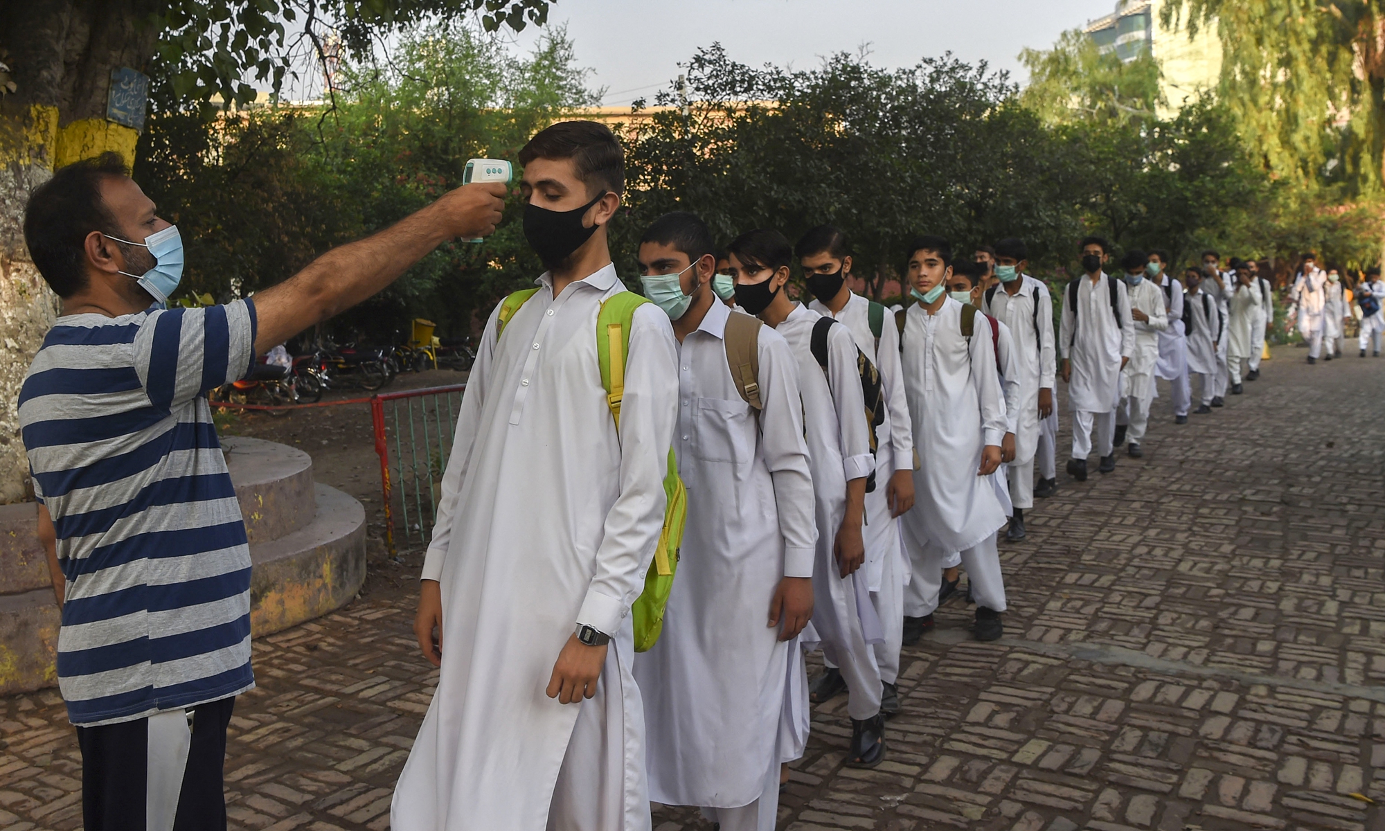 A teacher checks the temperature of a student as others stand in line upon their arrival at a school in Peshawar on Thursday, after the Pakistani government reopened schools closed as a preventive measure to curb the spread of the COVID-19. Photo: AFP