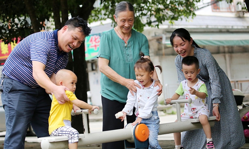 Three children play at a playground accompanied by their parents and grandparent. Photo: VCG