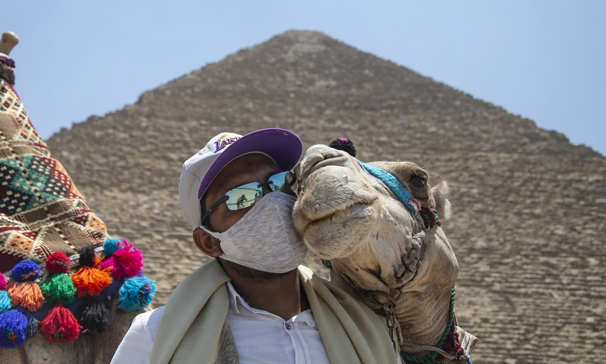 A man snuggles with a camel in front of the Giza Pyramids after the site was reopened for tourists in Giza, Egypt, on July 1, 2020. Photo: IC