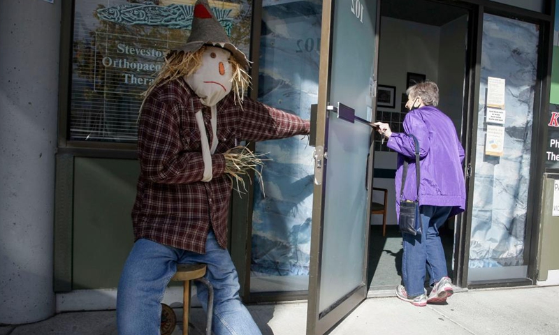 A scarecrow is displayed in front of a store at Steveston Village in Richmond, British Columbia, Canada, on Oct. 6, 2021. Scarecrows are created and placed outside stores at Steveston Village where people are encouraged to vote for the best designs of the year for Steveston Scarecrow Crawl competition.Photo:Xinhua
