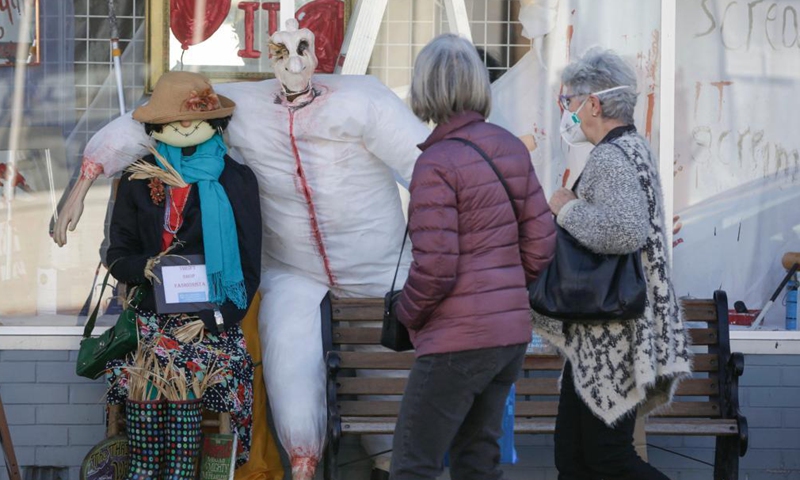 People walk past a scarecrow in front of a store at Steveston Village in Richmond, British Columbia, Canada, on Oct. 6, 2021. Scarecrows are created and placed outside stores at Steveston Village where people are encouraged to vote for the best designs of the year for Steveston Scarecrow Crawl competition.Photo:Xinhua
