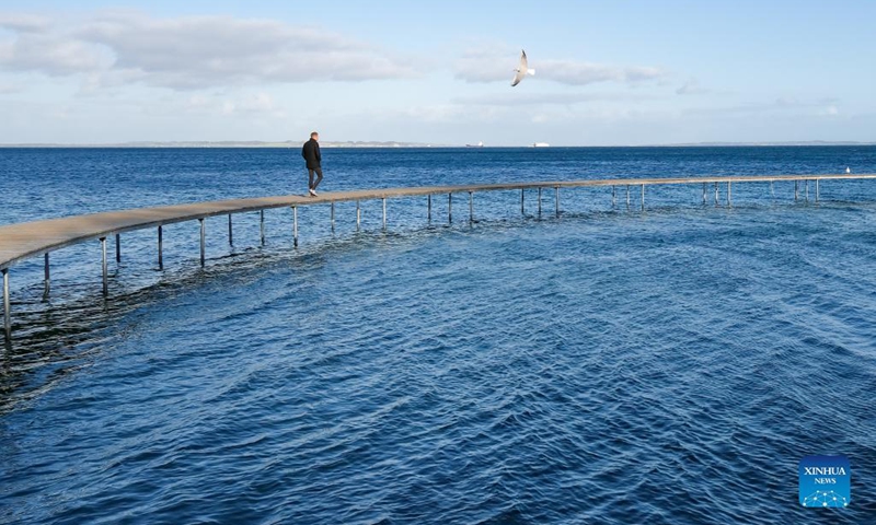 A man walks on The Infinite Bridge in Aarhus, Denmark, Oct. 11, 2021. The Infinite Bridge is a sculpture by Danish architect studio Gjode & Povlsgaard Arkitekter built at the beach in Aarhus. It has a diameter of 60 meters and is positioned half on the beach and half in the sea.(Photo: Xinhua)