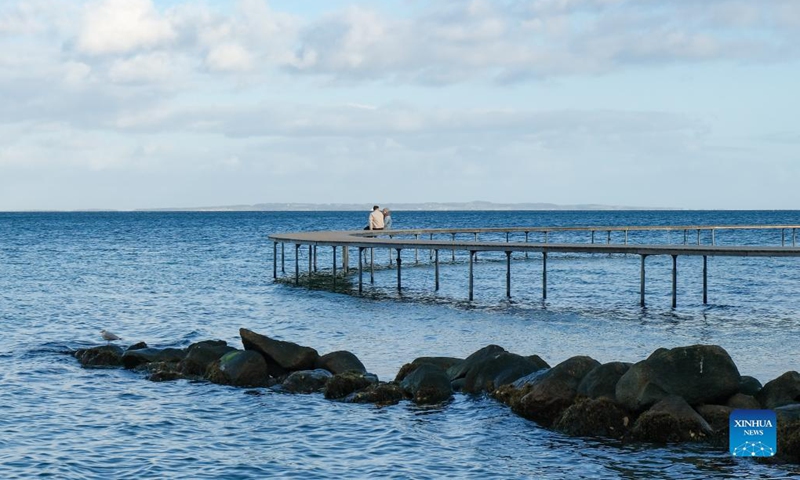 People sit on The Infinite Bridge in Aarhus, Denmark, Oct. 11, 2021. The Infinite Bridge is a sculpture by Danish architect studio Gjode & Povlsgaard Arkitekter built at the beach in Aarhus. It has a diameter of 60 meters and is positioned half on the beach and half in the sea.(Photo: Xinhua)