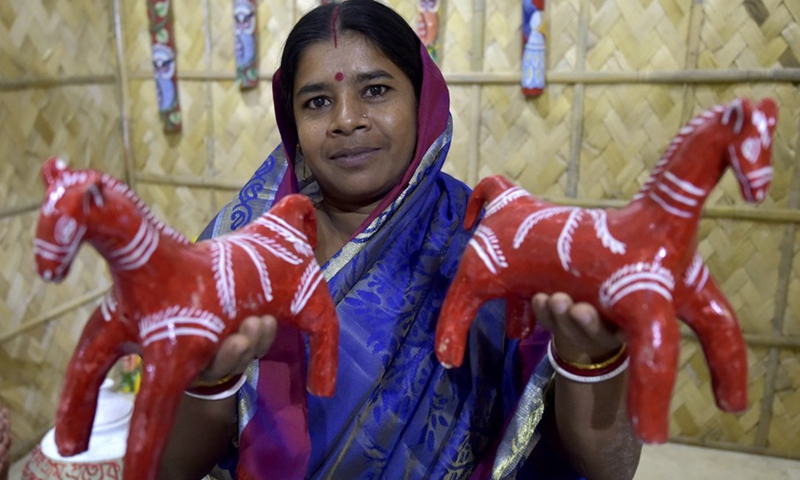 A woman shows clay horse showpieces during an exhibition featuring folk art and folk music in Dhaka, Bangladesh, Oct. 17, 2021.(Photo: Xinhua)