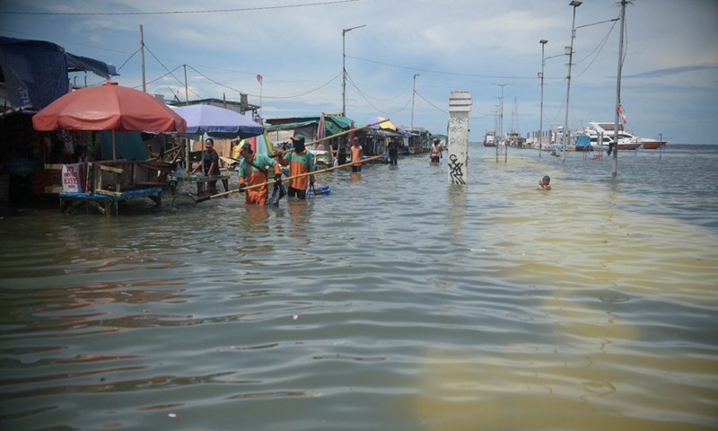 People walk in the flood water at a sea port on the coast of Jakarta, Indonesia, Nov. 9, 2021.(Photo: Xinhua)