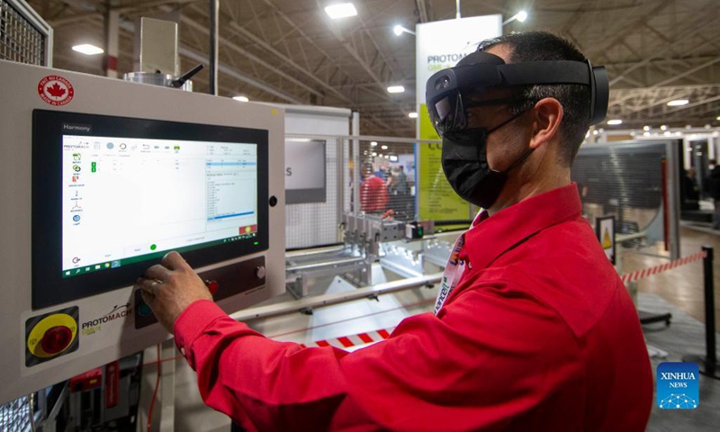 An exhibitor wearing mixed reality glasses (HoloLens 2) works on a machine during the 2021 WinDoor event in Toronto, Canada, on Nov. 17, 2021. Showcasing the window and door industry in Canada, the two-day event kicked off here on Wednesday.(Photo:Xinhua)