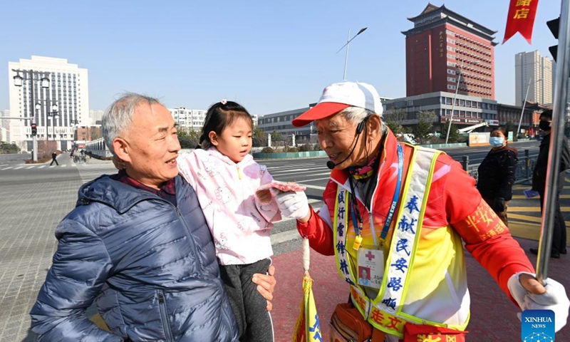 A passerby gives her sweets to octogenarian Ma Jinming as Ma directs traffic voluntarily in Taiyuan, capital of north China's Shanxi Province, Nov. 17, 2021. Ma Jinming, 80, has kept up voluntarily directing traffic on the street for eleven years. Photo: Xinhua
