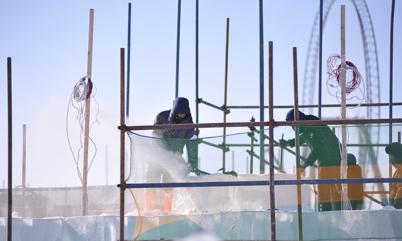 Workers lift ice bricks and machines produce artificial snow at the Harbin Ice and Snow World, in Harbin, Northeast China's Heilongjiang Province on December 1, 2021. The 2021 theme will incorporate elements of the Beijing 2022 Winter Olympic Games. The number of super ice slides, the most popular tourist attraction, has increased to eight, with the longest stretching 428 meters. Photo: VCG