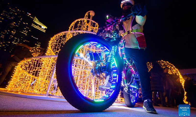 A man riding a bicycle decorated with LED lights poses for photos in front of a light installation during the 2021 Cavalcade of Lights in Toronto, Canada, Nov. 27, 2021.Photo:Xinhua