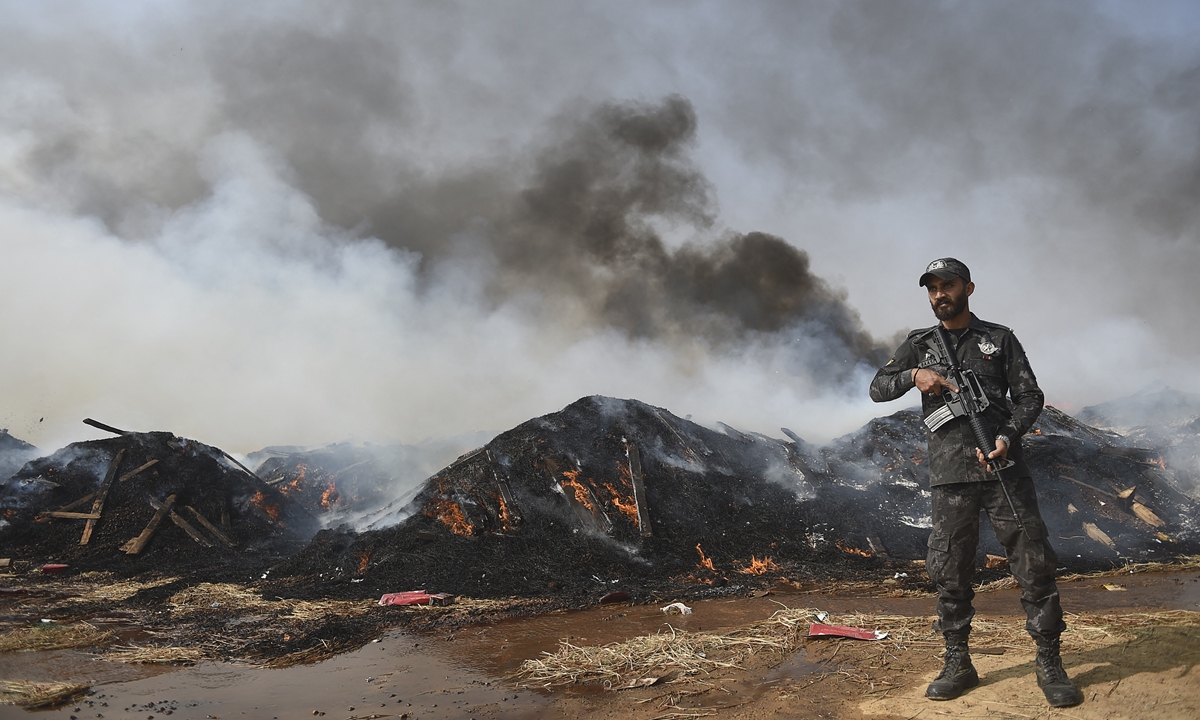 a customs official stands guard beside a burning pile of seized