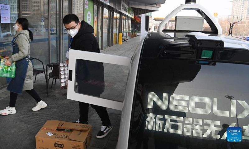 A convenience store owner picks up goods transported via an unmanned delivery vehicle in Xi'an, capital of northwest China's Shaanxi Province, Jan. 9, 2022. The driverless vehicle is designed to transport goods with a maximum weight of 320 kg per trip. It can traverse 6.5 km through the lanes on roads on a single trip. (Xinhua/Tao Ming)