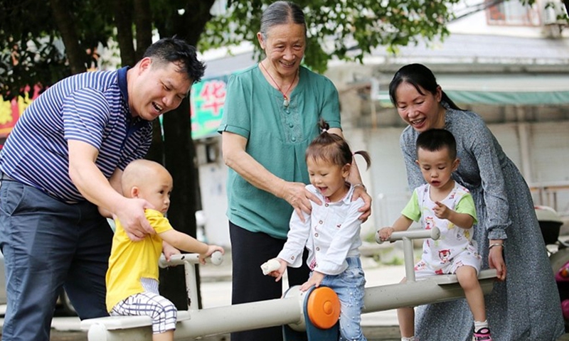 Three children play in a playground accompanied by their parents and grandparent. Photo: VCG