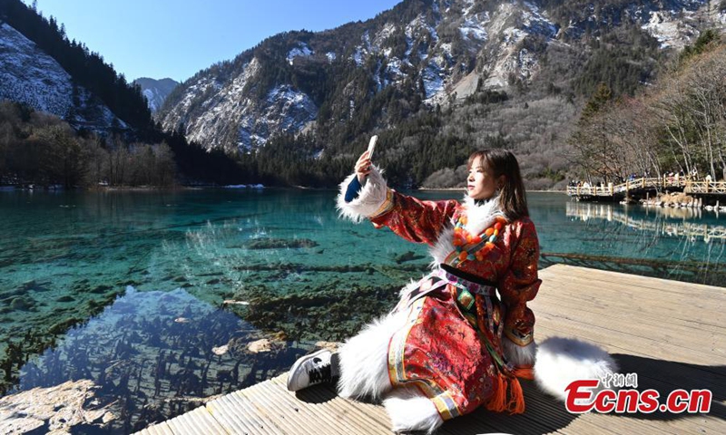 A tourist wearing ethnic costumes takes selfies at Jiuzhaigou National Park in the Aba Tibetan and Qiang Autonomous Prefecture, southwest China's Sichuan Province, Jan. 5, 2022. (Photo by An Yuan)