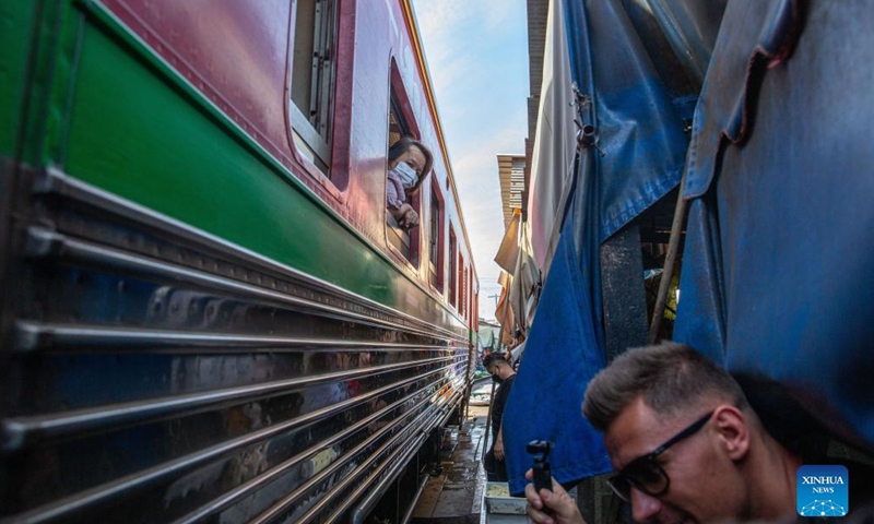 A commuter train runs through Maeklong Railway Market in Samut Songkhram Province, Thailand, Jan. 5, 2022. In Maeklong Railway Market, built along a railway track, a compromise is reached between vendors and passing commuter trains. When the rail track is clear, stall owners can set up stalls at will. Before the COVID-19 pandemic, the market had attracted many tourists.(Photo: Xinhua)
