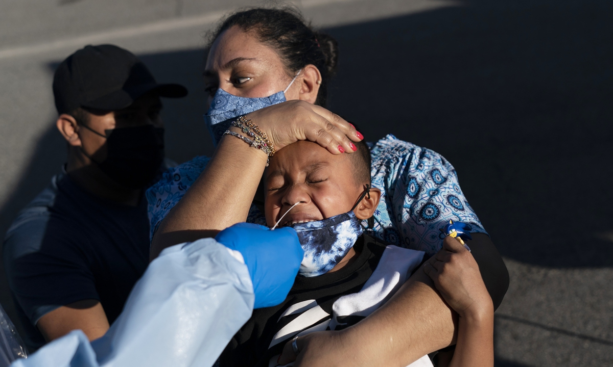A woman holds the head of her 6-year-old son as a nurse collects a nasal swab sample for a COVID-19 test in Tustin, California on January 6. The US is reporting six positive cases each second while the global cases crossed the 300 million mark on January 7. Photo: VCG