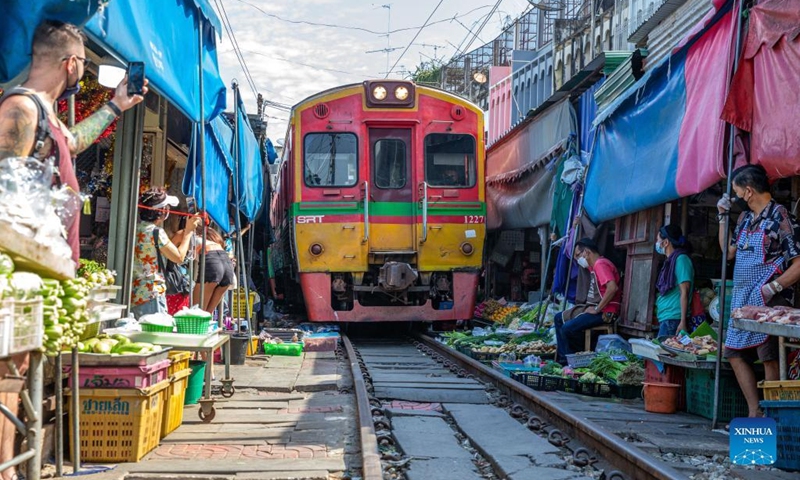 A commuter train runs through Maeklong Railway Market in Samut Songkhram Province, Thailand, Jan. 5, 2022. In Maeklong Railway Market, built along a railway track, a compromise is reached between vendors and passing commuter trains. When the rail track is clear, stall owners can set up stalls at will. Before the COVID-19 pandemic, the market had attracted many tourists.(Photo: Xinhua)
