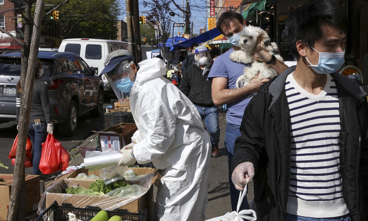 In the Chinese community in Brooklyn, New York, a street vendor wears protective a suit to sell vegetables with pedestrians in masks and other personal protection equipment on May 12, 2020. Photo: VCG