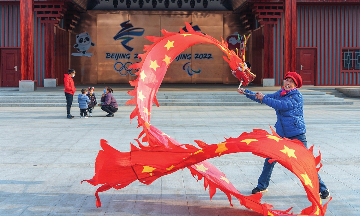 Una mujer practica la danza tradicional de cintas de colores frente a una pared decorada con emblemas olímpicos en una comunidad del distrito de Shijingshan, Beijing, el 11 de enero de 2022. Foto: Li Hao/GT 