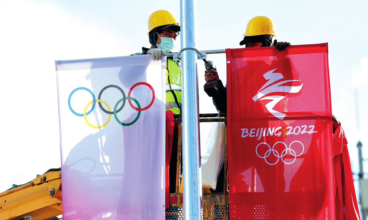Workers hang banners with logos of Olympic Games and Beijing 2022 Winter Olympic Games by a road in Beijing on January 10, 2022. Photo: VCG