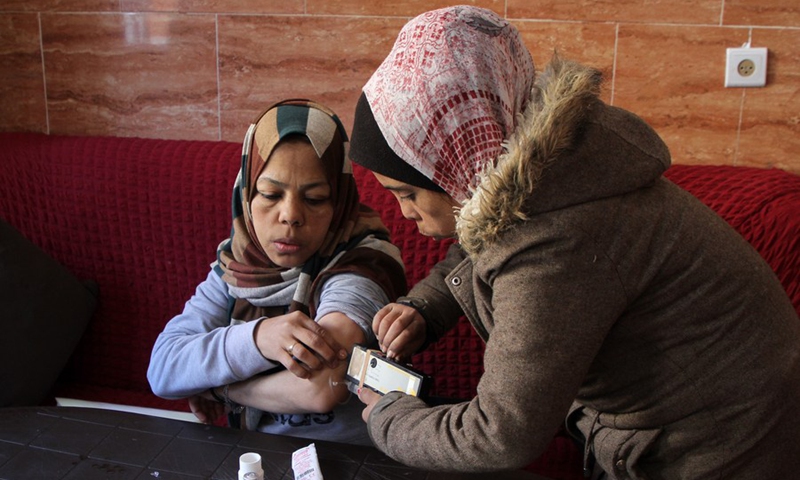 Palestinian thalassemia patient Sawsan al-Masri (R) helps her sister Falastin (L) with her medicine at their house, in the northern Gaza Strip town of Beit Hanoun, on Jan. 17, 2022.(Photo: Xinhua)