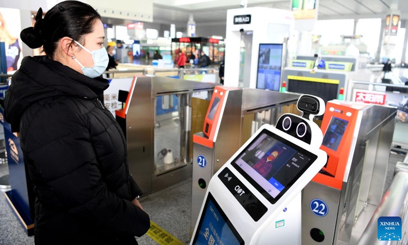 Da Bai (R), an intelligent temperature measuring robot, measures a passenger's body temperature at the entrance of Hefei South Railway Station in Hefei, east China's Anhui Province, Jan. 18, 2022. Air environment automatic sterilizer robot Xiao Chuang, intelligent temperature measuring robot Da Bai and ground cleaning and disinfecting robot Xiao De have been in service for COVID-19 prevention and control during the annual Spring Festival travel rush in Hefe(Photo: Xinhua)