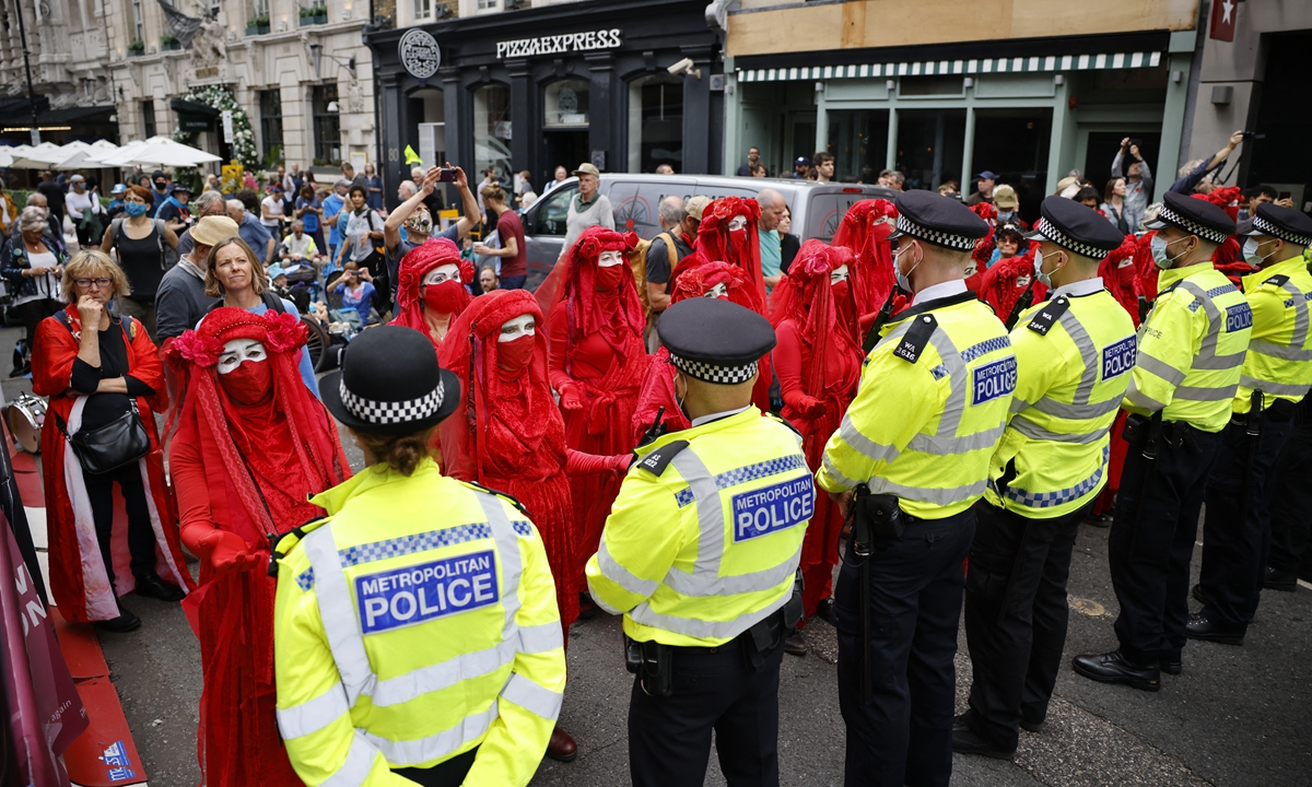 Members of the Red Rebel Brigade - an international performance artivist troupe - face a cordon of police officers as they join climate activists from the Extinction Rebellion group in central London on August 23, 2021. Photo: AFP