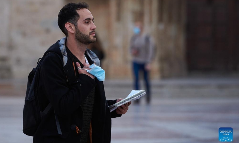 A man with a mask on his hand walks in downtown Valencia, Spain, on Feb. 11, 2022.Photo:Xinhua