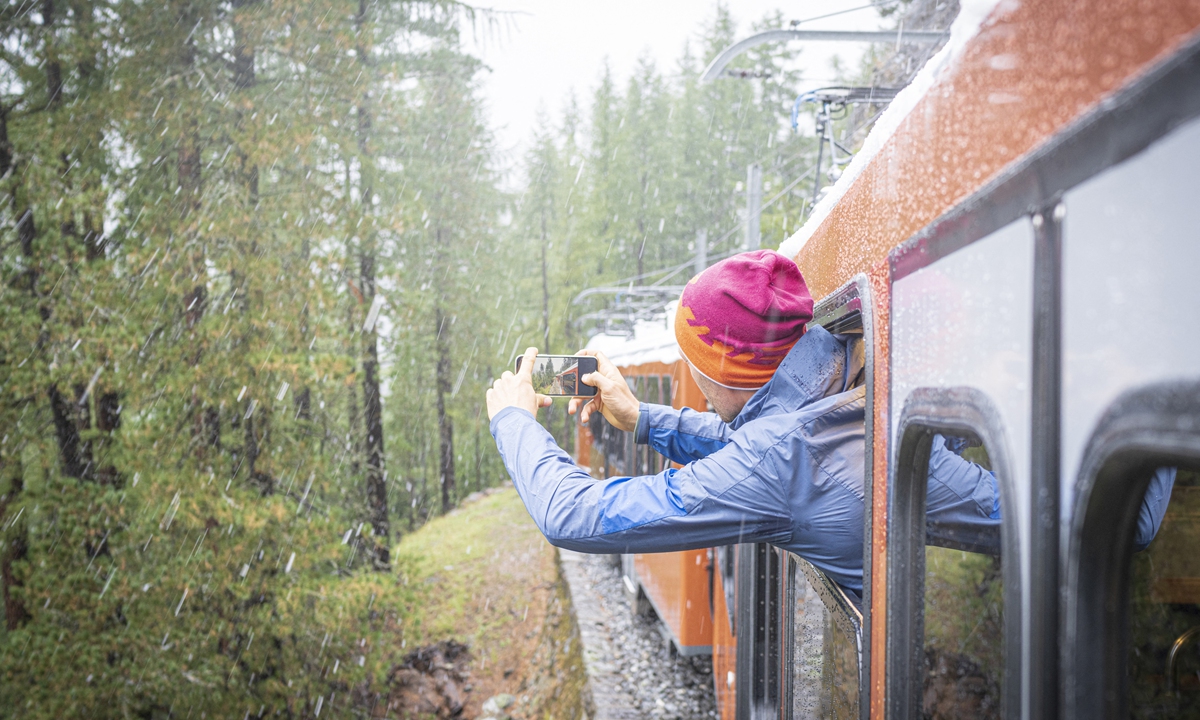 A man takes a photo of the snow falling over the forest leaning out of Gornergrat Bahn train, Zermatt, Switzerland. Photo: AFP