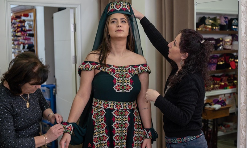 Palestinian fashion designer Khawla al-Tawil (R) helps a model put on one of her designs at her store in the West Bank town of Beit Sahour on Feb. 9, 2022. (Photo: Xinhua)