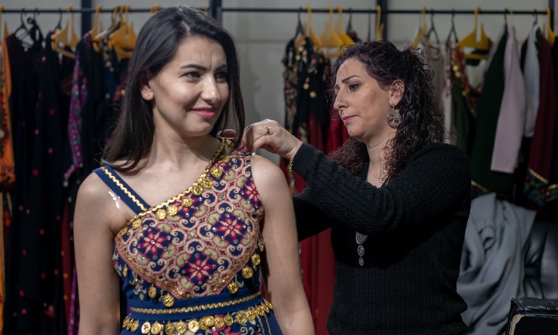 Palestinian fashion designer Khawla al-Tawil (R) helps a model to put on one of her designs at her store in the West Bank town of Beit Sahour, on Feb. 9, 2022.(Photo: Xinhua)