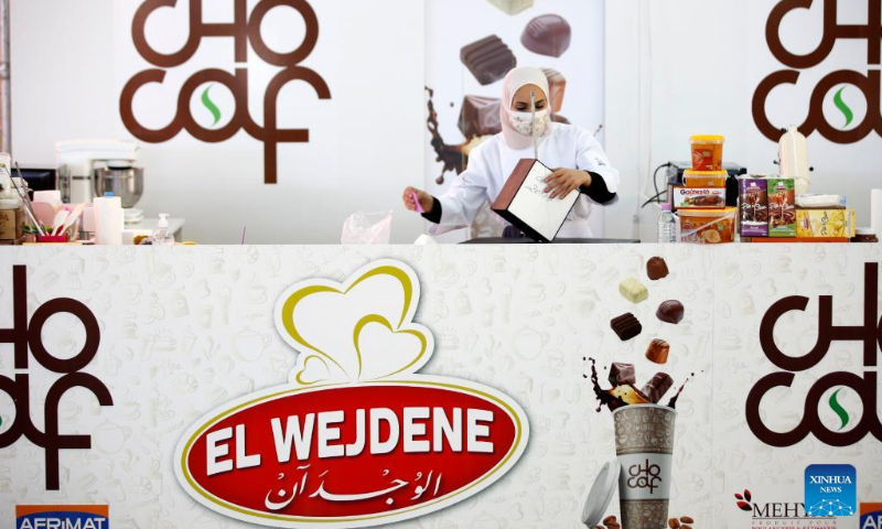 An exhibitor arranges products during the Algerian International Fair of Chocolate and Coffee (Chocaf) in Algiers, Algeria, on Feb. 19, 2022. From Feb. 18 to Feb. 21, coffee and chocolate lovers, experts and international producers gather in Algiers to participate in the 5th edition of Chocaf. (Xinhua)