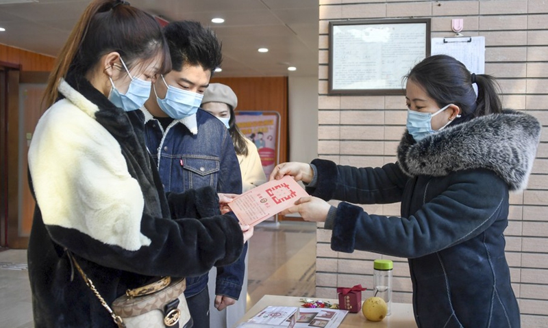 A staff member (R) presents a commemorative card to a couple at a marriage registry of Haidian District in Beijing, capital of China, Feb. 22, 2022.(Photo: Xinhua)