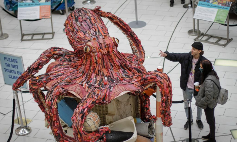 People look at an octopus art sculpture made of plastic marine debris during the 