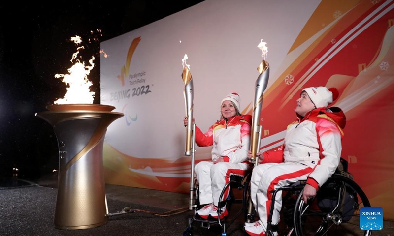 Torch bearers Aileen Neilson (R) and Angie Malone, wheelchair curlers, hold their torches during the Paralympic Heritage Flame Lighting Ceremony for the Beijing 2022 Winter Paralympic Games in Stoke Mandeville, Britain, Feb. 28, 2022. Photo: Xinhua