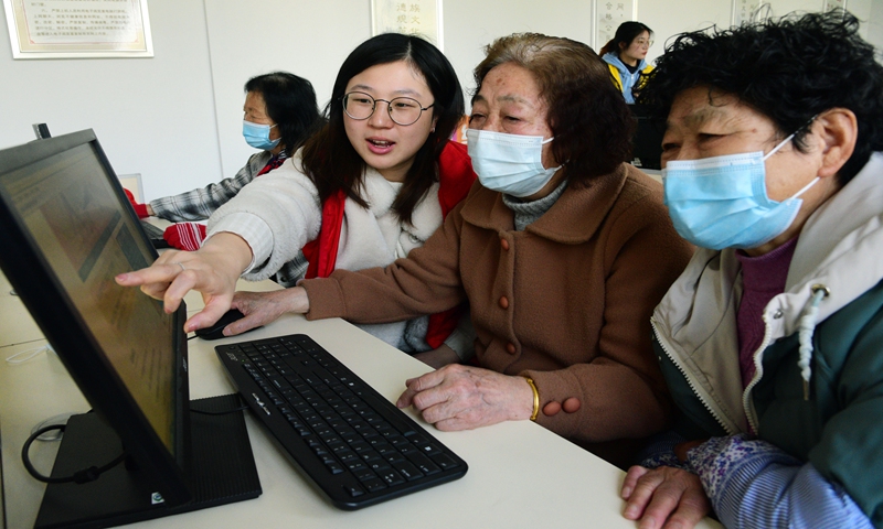 Volunteers from Jiangsu University help the elderly browse news about the two sessions online in Zhenjiang, East China's Jiangsu Province on March 8, 2022. Older people are using computers and smartphones to read about old-age security, medical care policies, and services for the elderly discussed at the two sessions. Photo: VCG