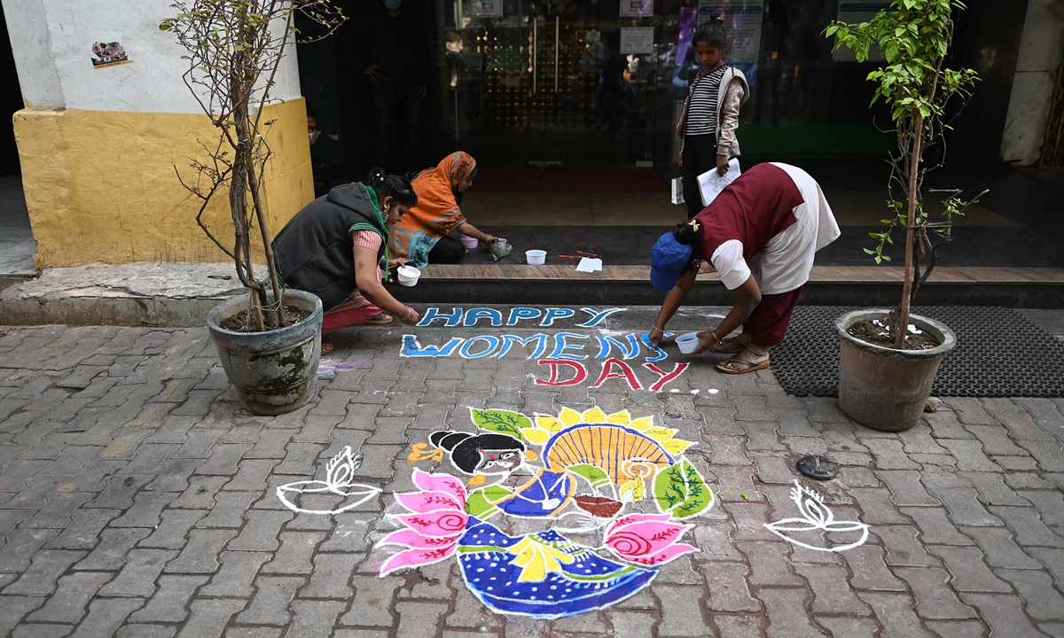 Staff members (front) apply colored powder to a rangoli (traditional floor decoration) reading 