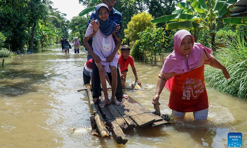 A woman pulls a wooden craft carrying her family in flood water after attending a wedding ceremony in Cilacap, Central Java, Indonesia, March 16, 2022.(Photo: Xinhua)