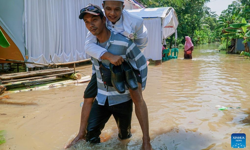 A man carrying a bridegroom wades through flood water after a wedding ceremony in Cilacap, Central Java, Indonesia, March 16, 2022.(Photo: Xinhua)