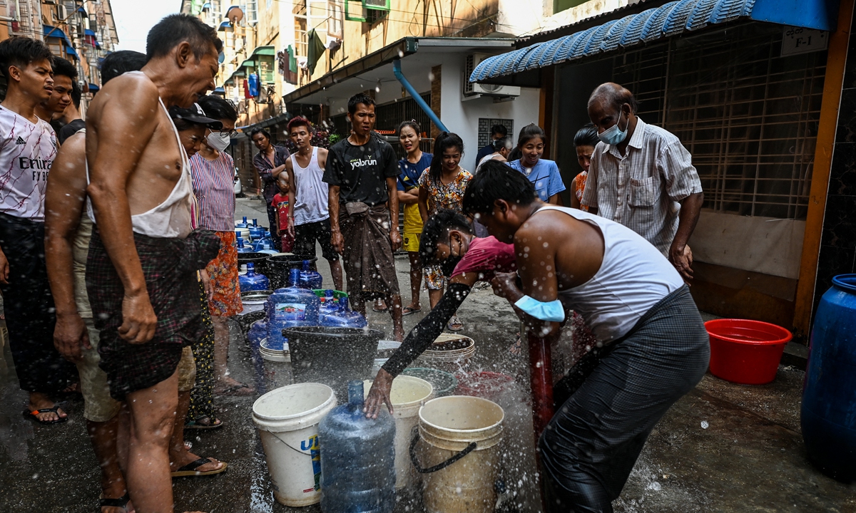 People react as water sprays while filling up containers in Yangon, Myanmar on March 14, 2022, as thousands of people face water shortages in the city. Photo: AFP