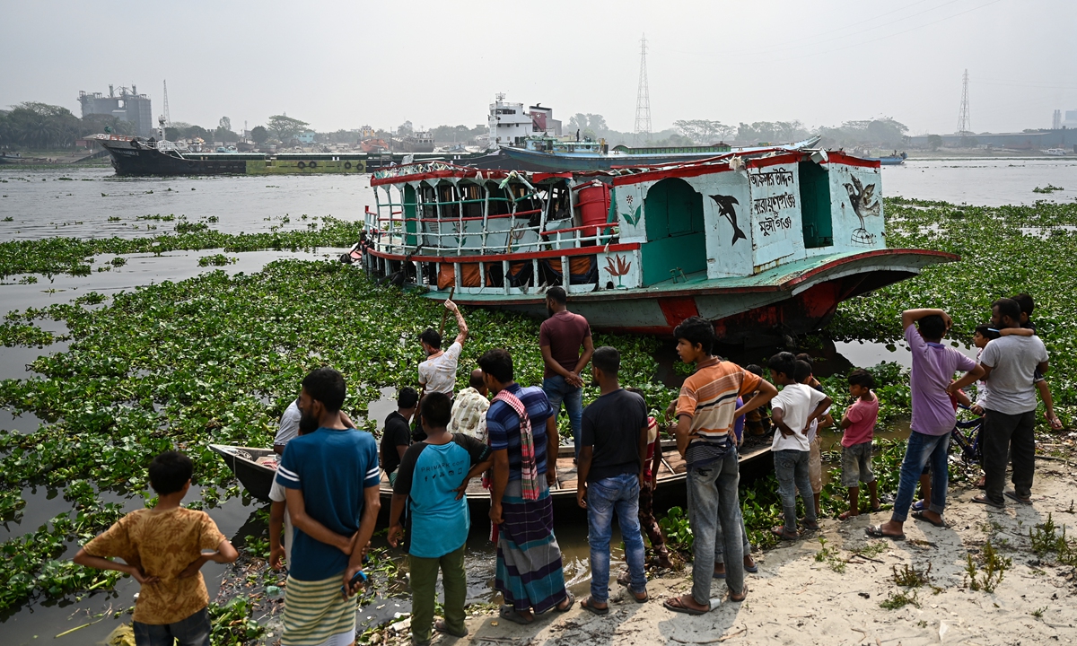 People watch the rescued ferry following an accident in the Shitalakshya River in Narayanganj, Bangladesh on March 21, 2022. At least six people are dead and dozens more are believed missing after a bulk carrier crashed into a small ferry in a river near Bangladesh's capital on March 20. Photo: AFP