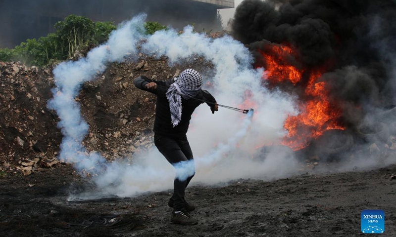 A Palestinian protester uses a slingshot to throw back a tear gas canister fired by Israeli soldiers during clashes after a protest against the expansion of Jewish settlements in Kufr Qadoom village near the West Bank city of Nablus, March 25, 2022.(Photo: Xinhua)